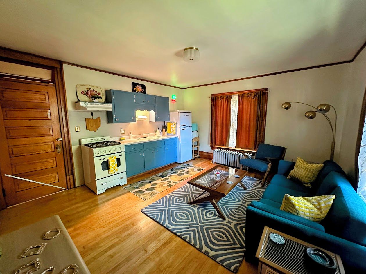 A compact living space with a kitchenette, a sofa set, and a patterned rug.