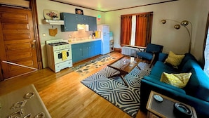 Un espace de vie compact comprenant un coin cuisine, un ensemble de canapés et un tapis à motifs.