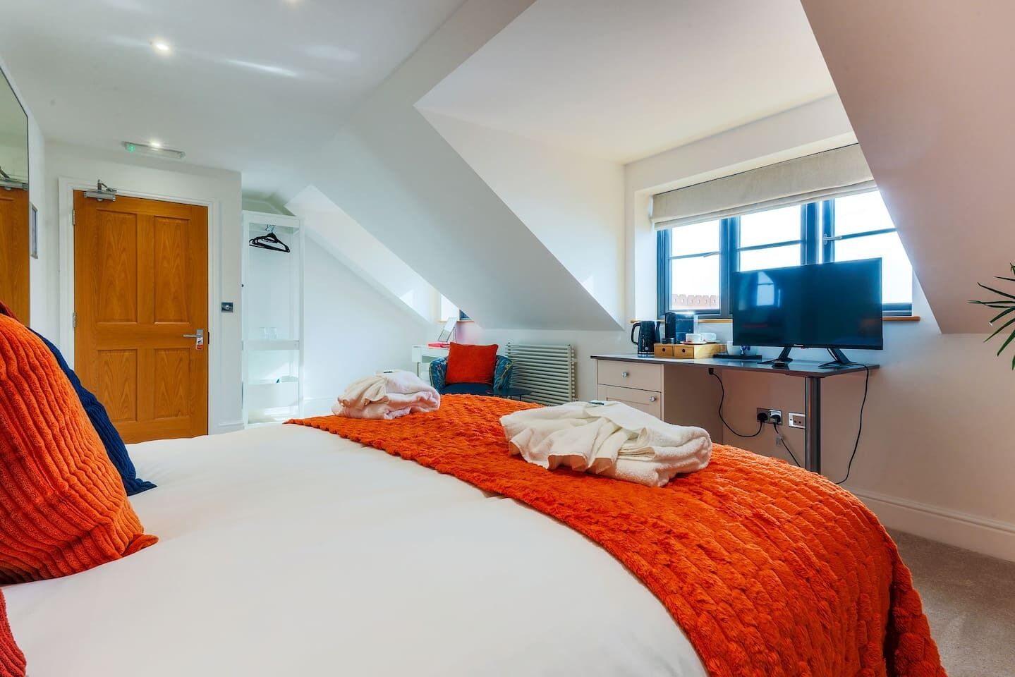 A bedroom with a bed, a desk with a computer, a window, and a radiator.