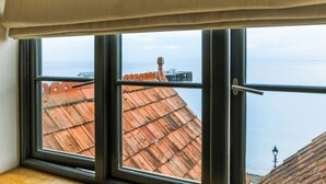 Ein Zimmer mit großem Fenster und Blick auf die Küste, mit einem Pier und einem Gebäude mit rotem Dach im Blickfeld.
