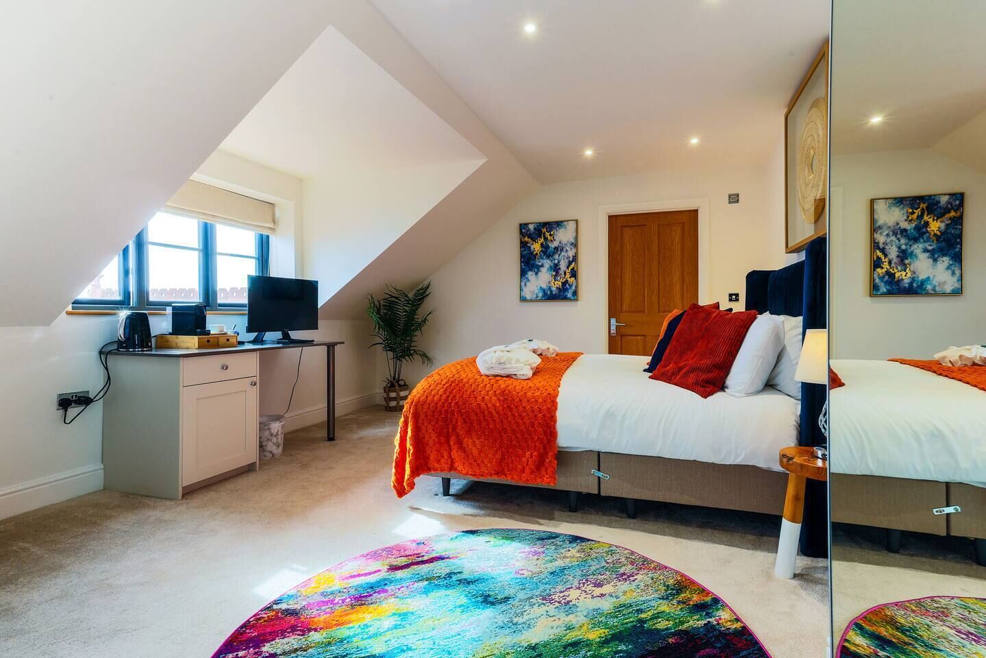 Une chambre à coucher avec un lit, un bureau, une chaise, une fenêtre et une plante.