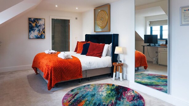 Ein modernes Schlafzimmer mit einem Bett, einem Spiegel, einem Schreibtisch und einem farbenfrohen Teppich.
