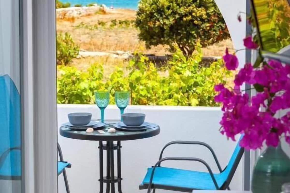 Un balcon avec une table, des chaises et une vue sur la mer et la verdure.