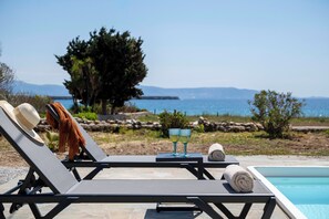 Un espace aménagé au bord de la piscine, avec des chaises longues, un chapeau, une serviette et deux verres posés sur une table.