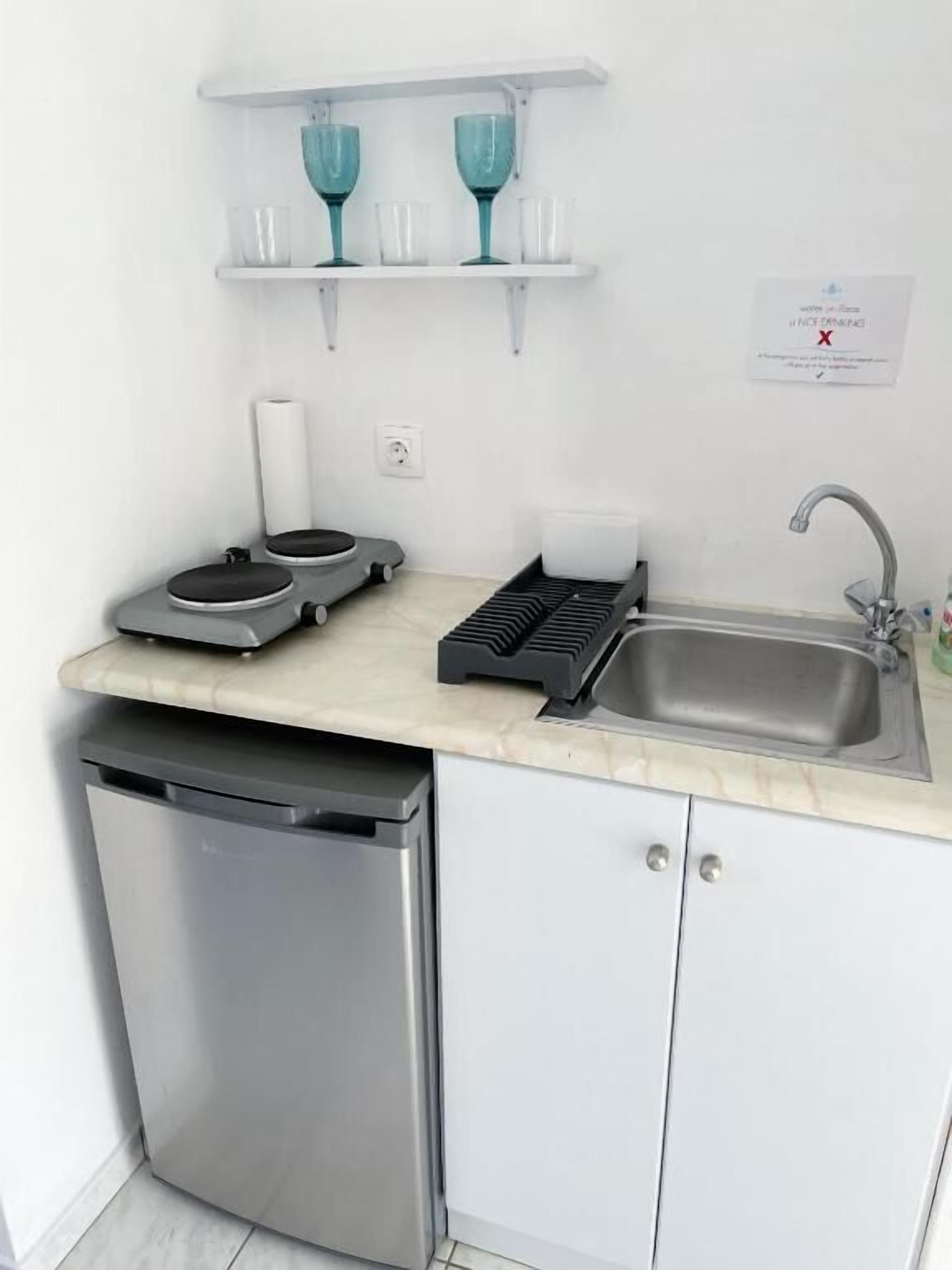 Een compacte keuken met een vaatwasser, een spoelbak, een aanrecht en een klein plankje met glazen.