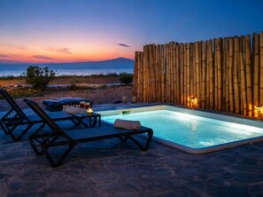 Un espace piscine avec des chaises longues et un mur en bambou, donnant sur une plage au crépuscule.