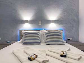 A hotel room with a bed, striped pillows, a headboard with built-in lighting, and a blue ambient light strip. - Villa Zeta (Paros)