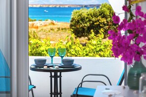 A balcony with a table set for two, a chair, and a vase with flowers. - Villa Zeta (Paros)
