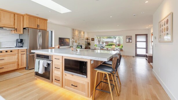 Een moderne keuken met houten kastjes, roestvrijstalen apparatuur, een marmeren aanrecht en een groot schiereiland met barkrukken.