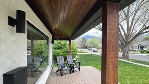 Een overdekt terras met houten vloer, twee Adirondack stoelen en een glazen wand met een zwarte lijst.