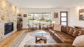 Een woonkamer met een stenen muur, een open haard, een leren bank, een glazen salontafel en uitzicht op de straat.