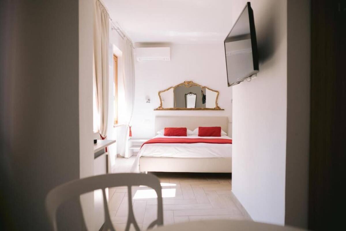 A hotel room with a bed, a TV mounted on the wall, a bedside table, and a chair.