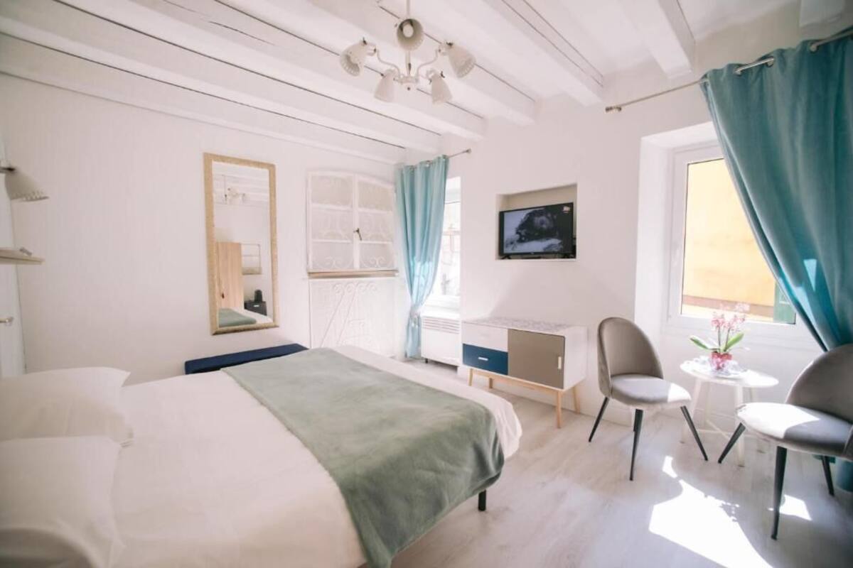 A bedroom with a bed, a desk, two chairs, a TV, and a window with curtains.