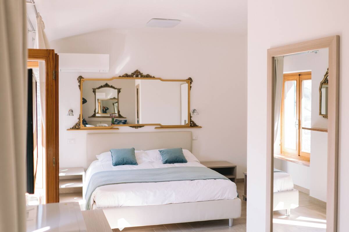 A bedroom with a bed, a mirror, a dresser, and a window.