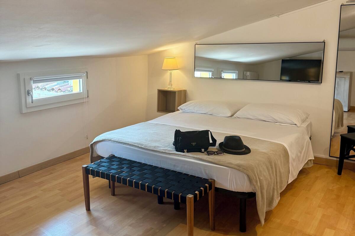 A bedroom with a bed, bench, lamp, and a large mirror.