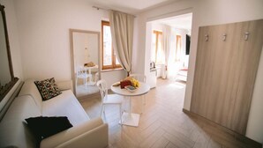 A modern living room with a sofa, a dining table with chairs, a kitchen area, and a wooden wardrobe. - Casa Cavour Garda (Garda)