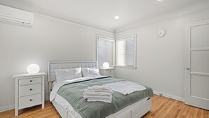 Ein Schlafzimmer mit einem Bett, Nachttischen, einer Wanduhr und einem Fenster mit Jalousien.