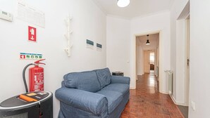 Ein Flur mit einem blauen Sofa, einem Feuerlöscher, einer Heizung und einer Deckenleuchte.