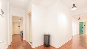 Ein Flur mit Holzdielen, weißen Wänden und einem Mülleimer.
