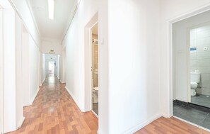 A hallway with wooden flooring, white walls, and a visible bathroom with a toilet and sink. - HOUZE Spacious 9 bedroom flat in Central Lisbon (Lisboa)