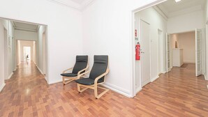 Ein Flur mit Holzboden, zwei schwarzen Stühlen, weißen Wänden und einem Feuerlöscher.