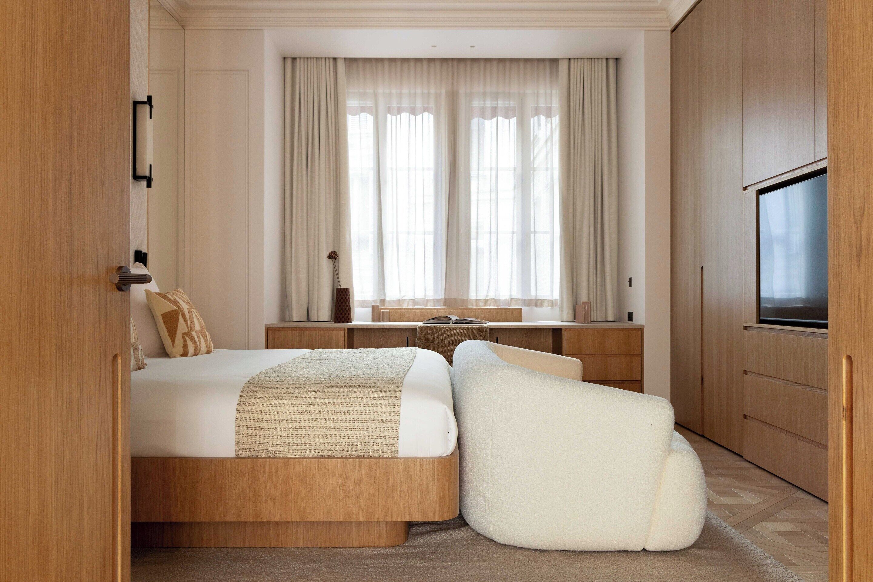 A modern hotel room with a bed, a desk, a TV, and a large window with curtains.