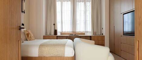 A modern hotel room with a bed, a desk, a TV, and a large window with curtains.