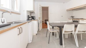 Una cocina moderna con armarios blancos, un comedor con sillas blancas y una puerta visible que conduce a otra habitación.