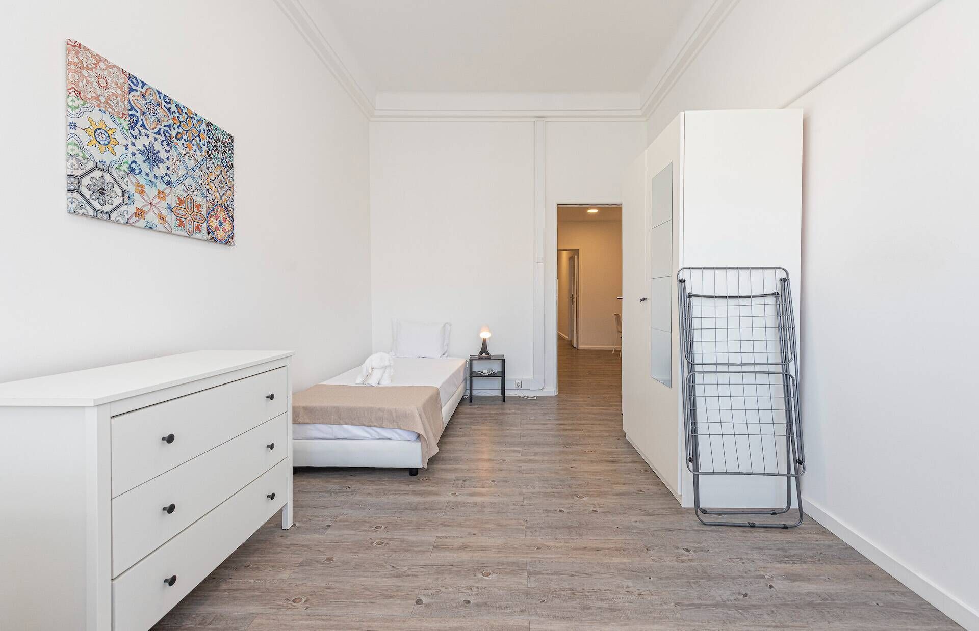 Une chambre à coucher comprenant un lit, une commode, une table de chevet, une lampe et un étagère en métal.