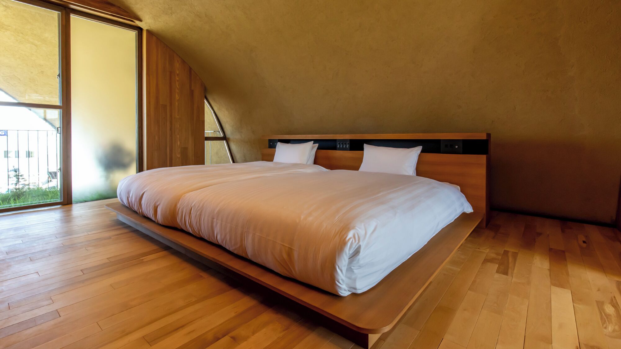 Un dormitorio con una cama grande, suelo de madera y techo inclinado.