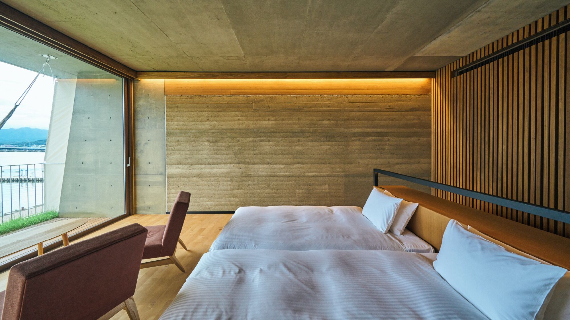 Una habitación de hotel moderna con una cama grande, un cabecero de madera y vistas al exterior.