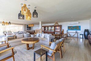 Ein großzügiger Wohnbereich mit einer großen Couch, Holzstühlen, einem runden Couchtisch und hängenden Korbschwingenlampen.