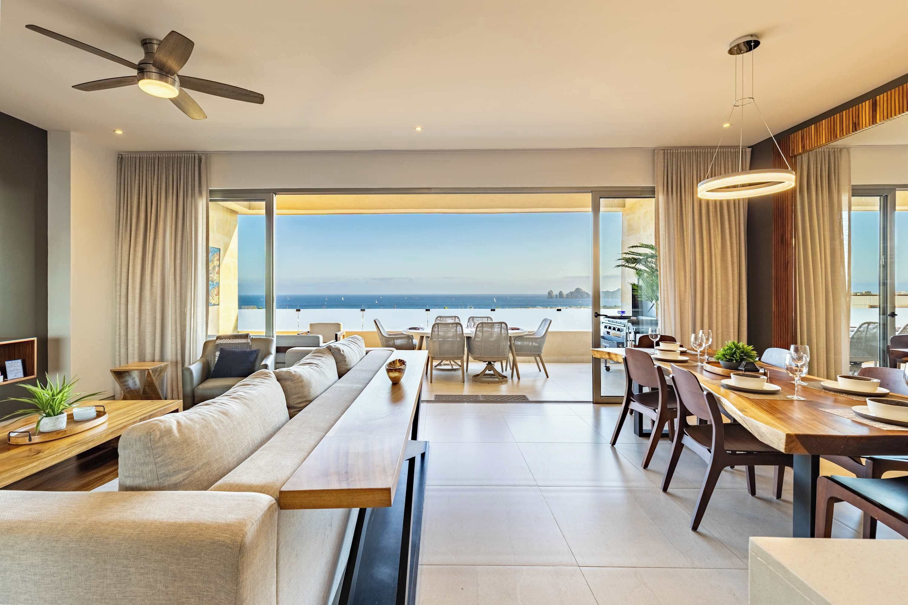 Un soggiorno moderno con divano, tavolo da pranzo e sedie, una ventola a soffitto e vista sull'oceano.