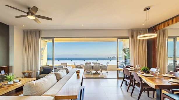 Een moderne woonkamer met een bank, eettafel en stoelen, een plafondventilator en uitzicht op de oceaan.