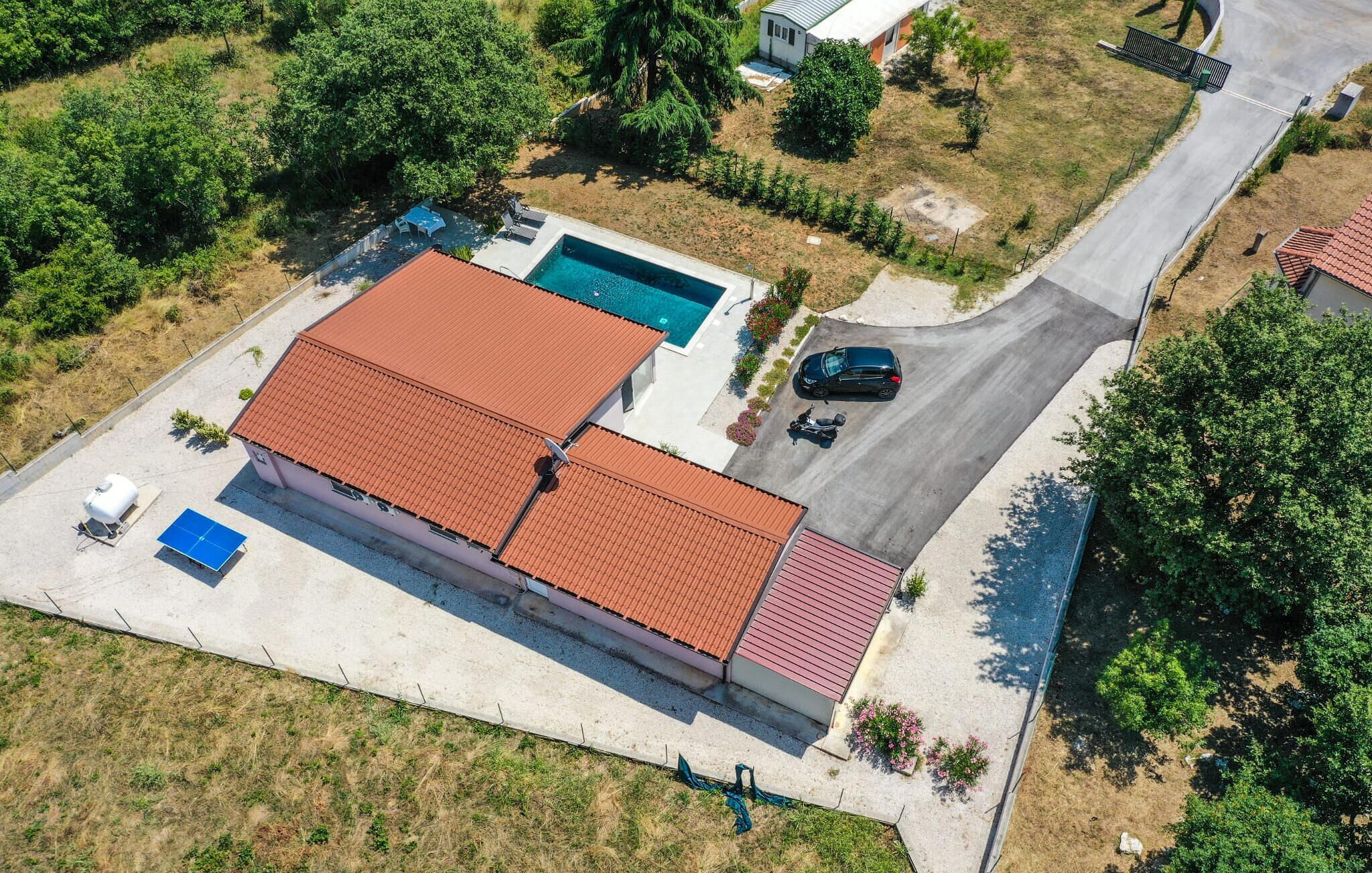 An aerial view of a residential property with a swimming pool, a covered patio, and a vehicle parked in the driveway.
