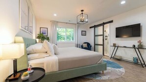 Ein Schlafzimmer mit Bett, Nachttisch, Lampe, Fenster und Fernseher an der Wand.