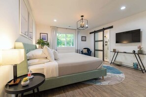 A bedroom with a bed, bedside table, lamp, window, and a TV on the wall. - 5-acres, 2 Cabins, Hot Tub, Sauna, Game Rm, Trails (Grapeview)