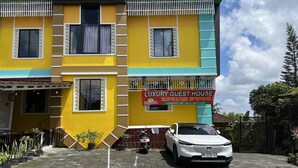 A multi-story building with a sign for 'Luxury Guest House' featuring amenities like a big room, clean, refrigerator, smart TV, Wi-Fi, and AC. - Stylish Double Suite with Balcony & Open Views (Bali)