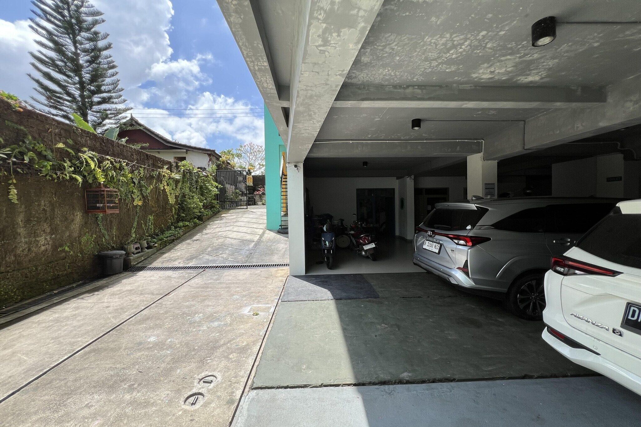 A parking garage with a white car and a silver SUV, a motorcycle, and a concrete wall with vegetation.