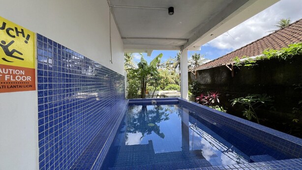 A swimming pool with blue tiles, a caution sign on the wall, and a view of the sky and plants. - Stylish Double Suite with Balcony & Open Views (Bali)