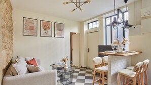 Cozinha moderna com piso xadrez, área de bar com banquetas e mesa de jantar com cadeiras. Há quadros nas paredes e um lustre sobre a cozinha.
