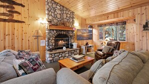 A cozy cabin interior with a stone fireplace, wooden walls, a comfortable sofa, and a television. - Meandering moose (Big Bear Lake)