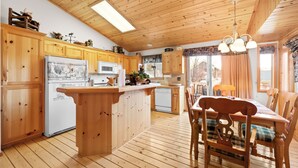 A wooden cabin interior with a kitchen, dining area, and a large window. - Meandering moose (Big Bear Lake)