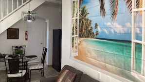 Ein Wohnzimmer mit einem Strandgemälde, eine Essecke mit Stühlen und einem Tisch, eine Treppe und ein Feuerlöscher.