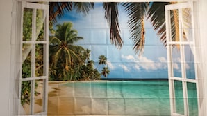 Strandbild durch ein Fenster mit Palmen und klarem Wasser.
