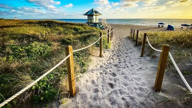 Un sentier de sable qui longe la plage et mène à un chalet de plage offrant une vue sur l’océan.