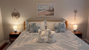 Un lit avec un motif de feuilles bleues et blanches, deux coussins en forme d’étoile de mer, une décoration murale en forme de cœur et un tableau encadré représentant une maison de plage.