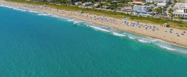 Vista aérea de una playa con numerosas sombrillas y una costa con edificios.
