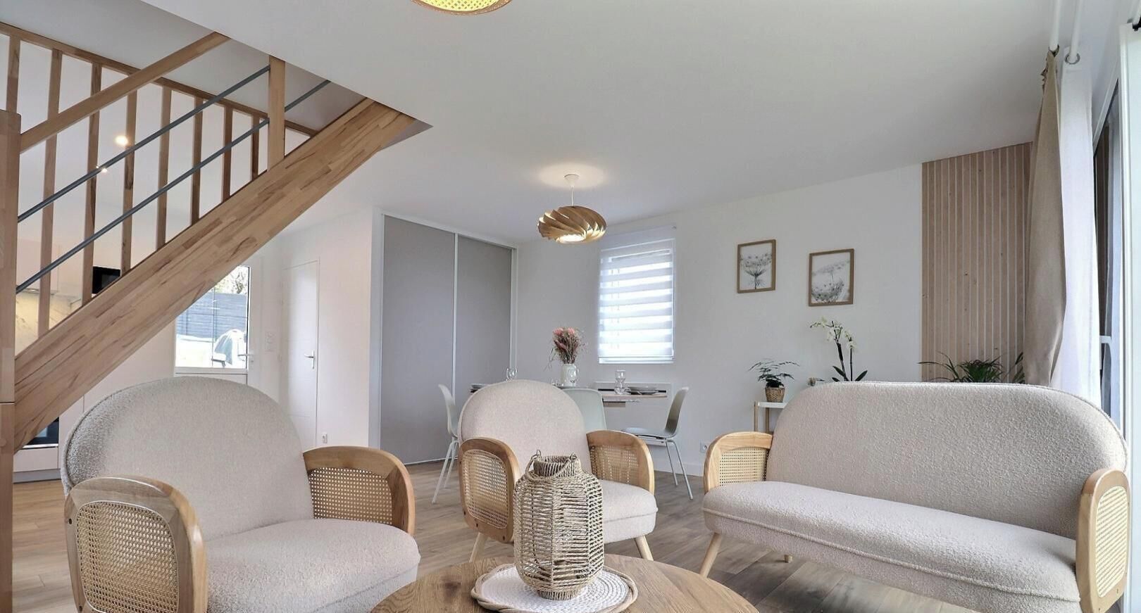 A modern living room with a wooden staircase, wicker furniture, and a dining area with a table and chairs.