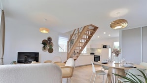Un salon moderne avec un téléviseur, des sièges, un escalier et un coin repas avec une table mise pour deux personnes.